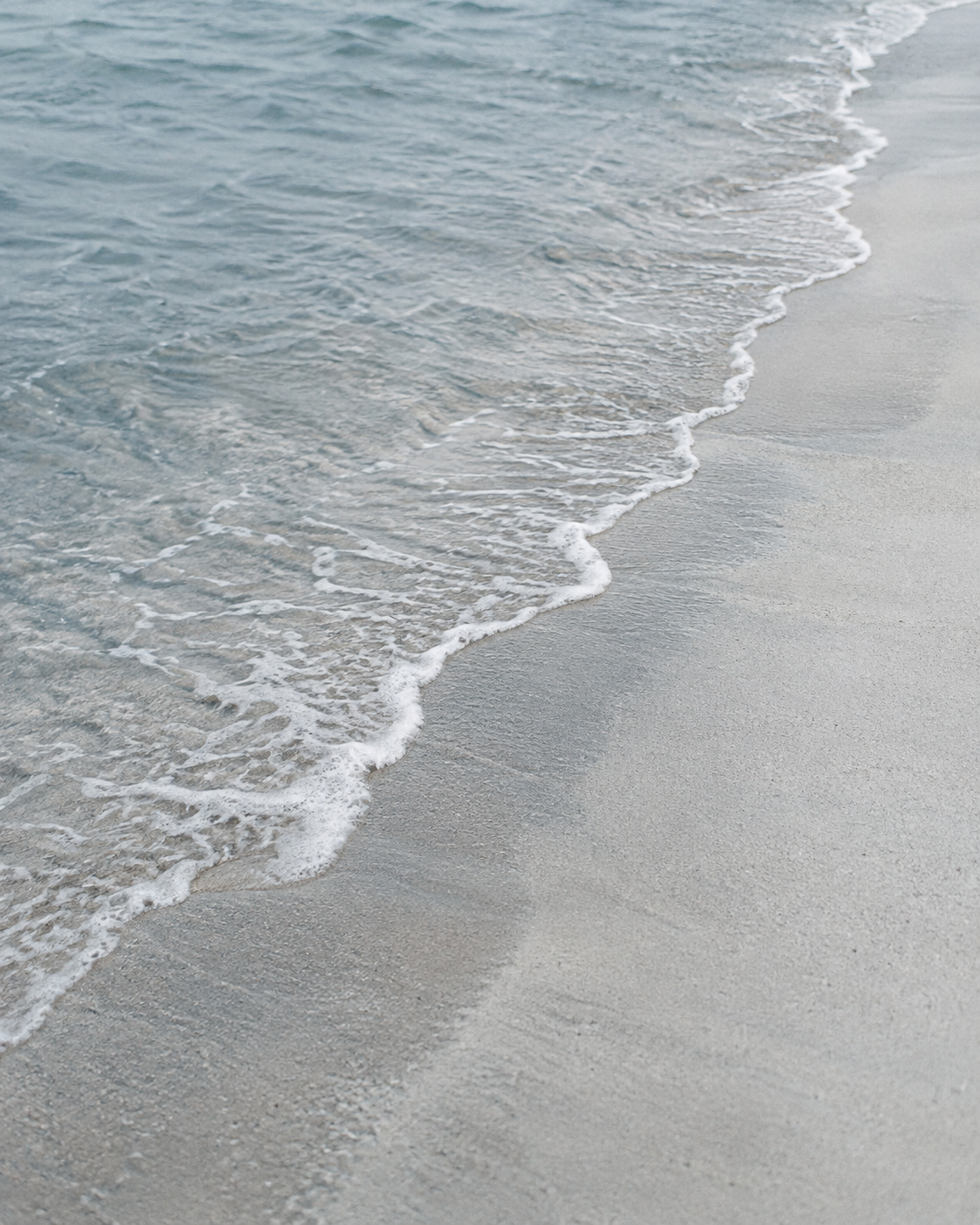 Eine helle Wasserlinie läuft diagonal über einen stillen Sandstrand.